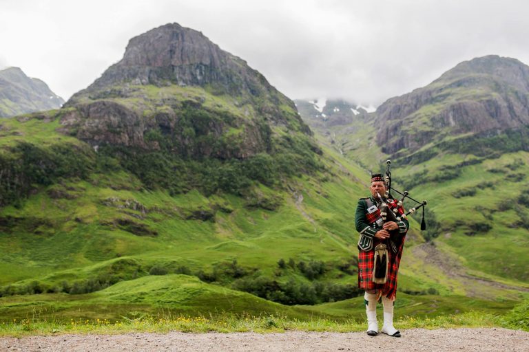 Man in kilt playing bagpipes in hills